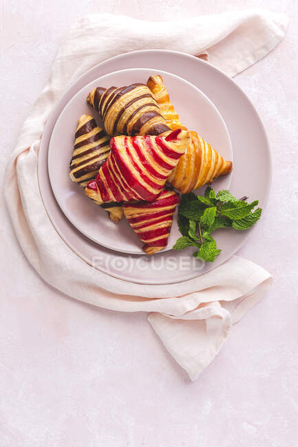 Vue de dessus de délicieux croissants placés sur une assiette avec un brin de menthe sur fond rose pastel — Photo de stock