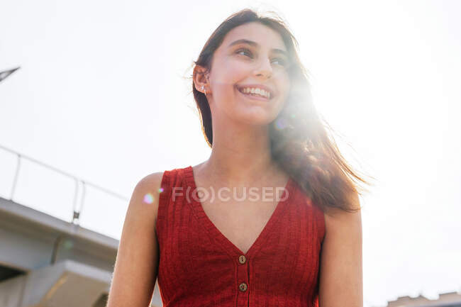 Low angle of young female in stylish glasses standing on background of bridge in city and looking away — Stock Photo