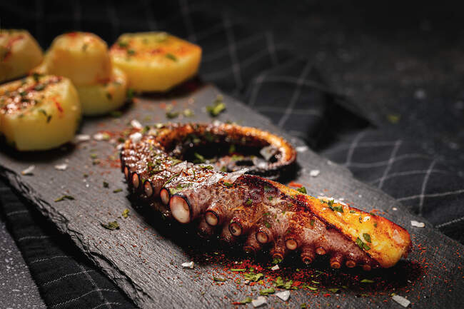 From above of fried octopus tentacle and pieces of potato served with spices on black board on table — Stock Photo