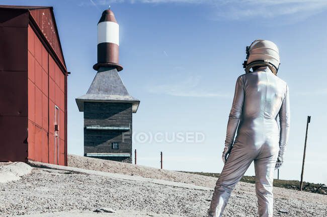 Вид сзади в скафандре, стоящем на раскаленной земле на фоне полосатой ракеты в солнечный день — стоковое фото