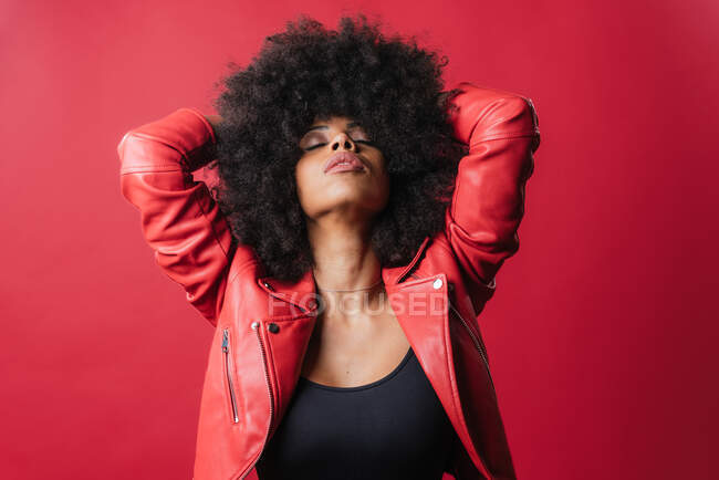 Traviesa afroamericana hembra gritando y tocando el pelo sobre fondo rojo en el estudio - foto de stock