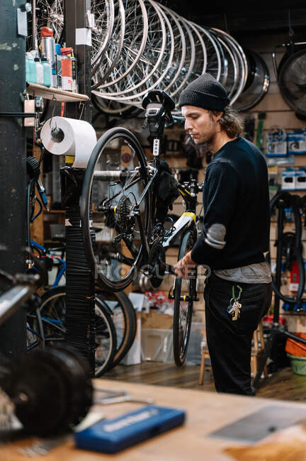 Vista laterale del serio meccanico maschio che ripara la ruota della bicicletta mentre lavora in officina — Foto stock