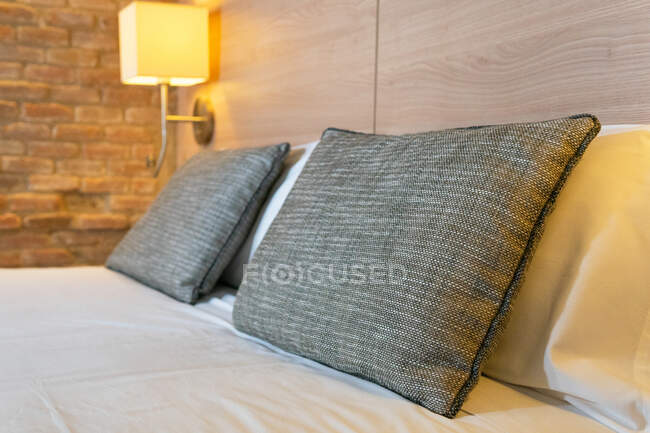 Інтер'єр спальні з м'якими подушками на ліжку з блискучими лампами, що висять на дерев'яному узголів'ї в готелі — стокове фото