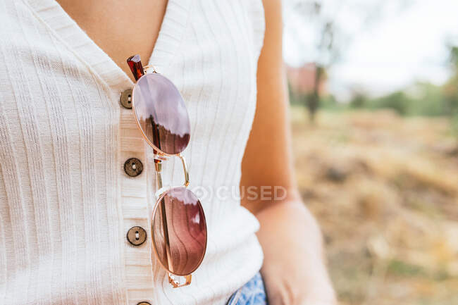 Vista lateral de una mujer anónima con gafas de sol colgando de su camisa - foto de stock