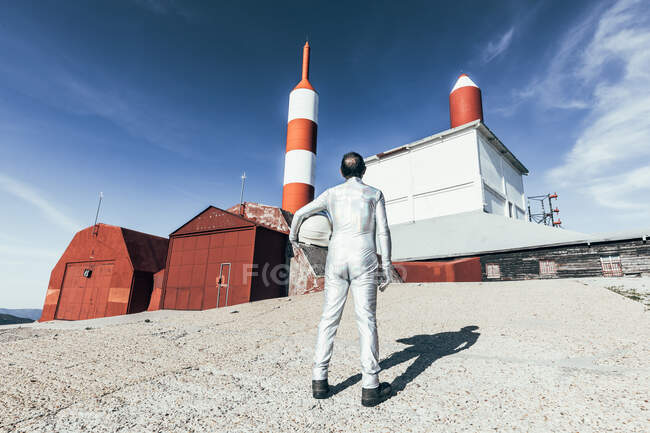 Back view an in spacesuit standing on rocky ground against striped rocket shaped antennas on sunny day — Stock Photo
