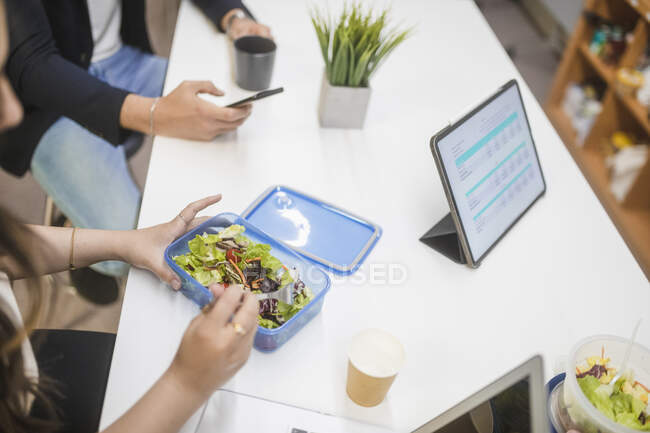 Von oben eine Gruppe unkenntlich gemachter Mitarbeiter, die sich am Tisch oder beim Mittagessen am Arbeitsplatz versammeln — Stockfoto