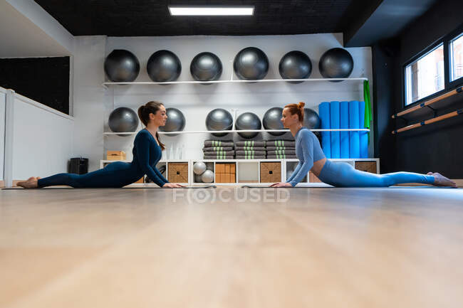 Vista laterale del corpo pieno di giovani donne in activewear che eseguono posa High Cobra durante la sessione di yoga in palestra — Foto stock
