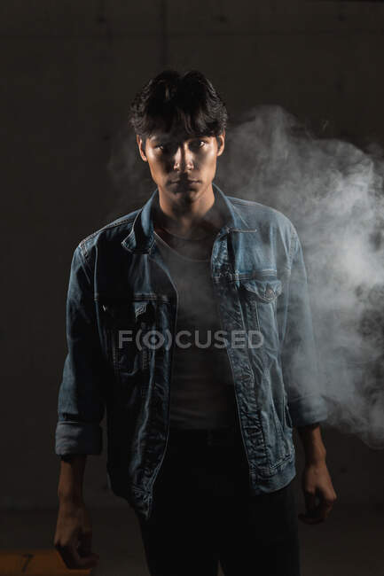 Retrato de jovem latino olhando com confiança para a câmera em meio a fumaça sob iluminação dramática — Fotografia de Stock