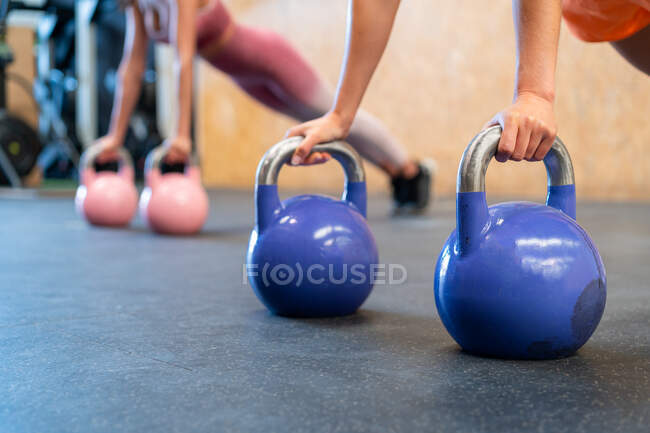 Cropped unrecognizable determined female athletes in sportswear standing in plank pose during functional training with weights on floor in gym — Stock Photo