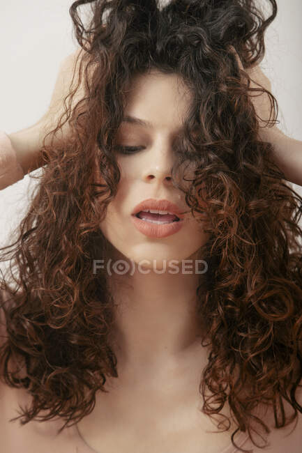 Femme sérieuse avec des cheveux frisés touchants et regardant vers le bas sur fond blanc en studio — Photo de stock