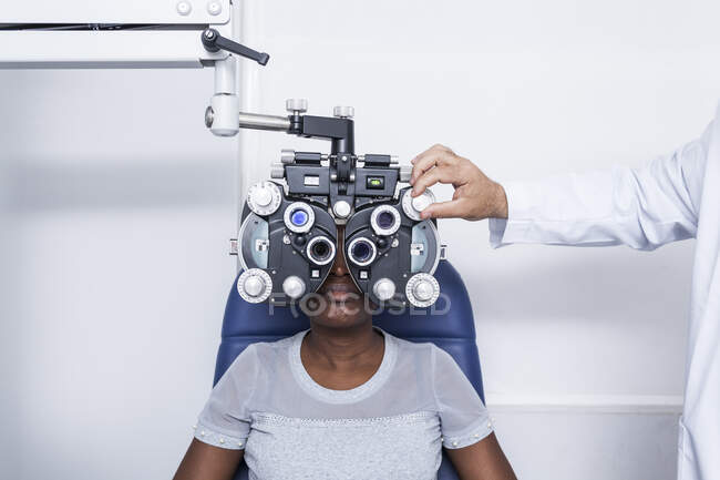 Optometrista ajustando el equipo de optometría durante el estudio de la vista de una mujer negra - foto de stock