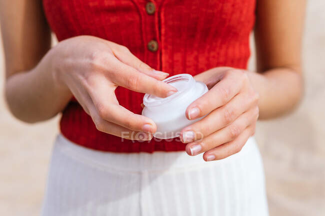 Crop anonymous female applying suntan lotion from glass jar on sunny day in summer — Stock Photo