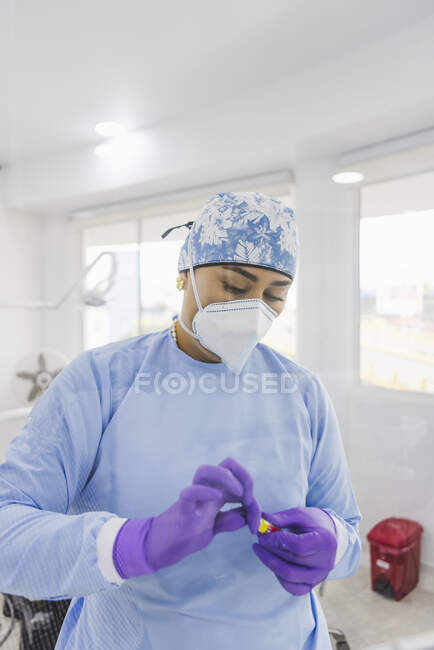 Adult female doctor in uniform and respiratory mask opening tube in hospital with shiny lamps — Stock Photo