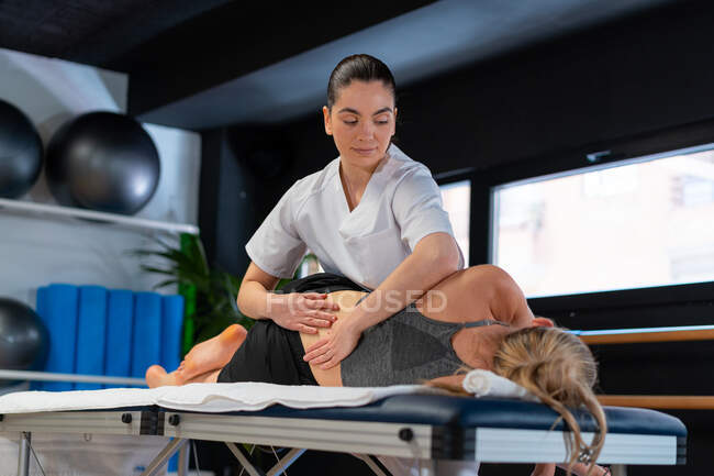 Женщина-терапевт в белом халате массирует спину женщине во время сеанса остеопатии в клинике — стоковое фото