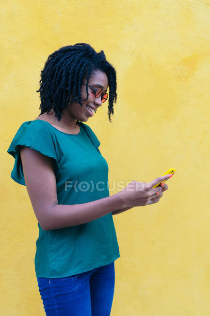 Retrato de una joven africana enviando mensajes de texto con un smartphone en la calle. - foto de stock