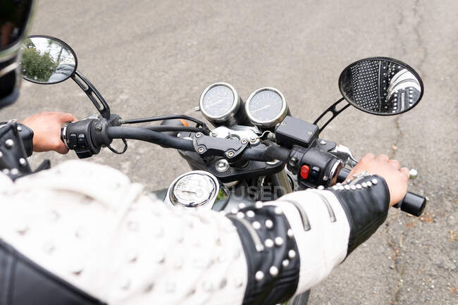 Cortar motociclista masculino em jaqueta de couro preto e capacete montando moto moderna na estrada de asfalto em meio a árvores verdes exuberantes crescendo no vale montanhoso — Fotografia de Stock