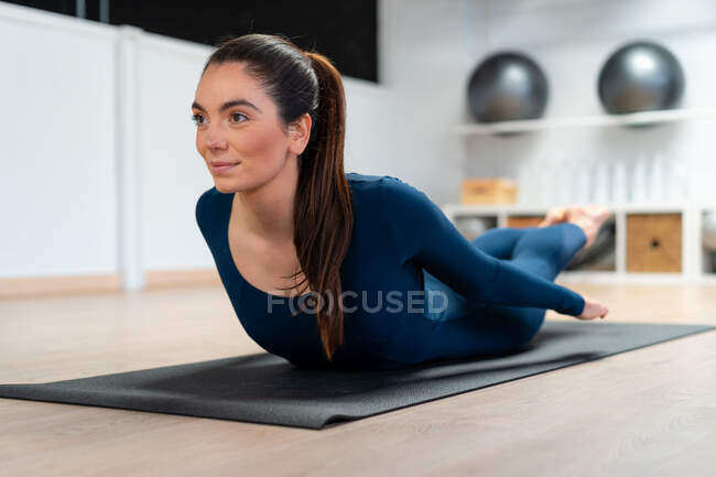 Full body of young female doing Locust pose while practicing yoga in studio looking away — Stock Photo