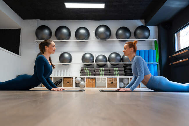 Full body side view of young females in activewear performing High Cobra pose during yoga session in fitness studio — Stock Photo