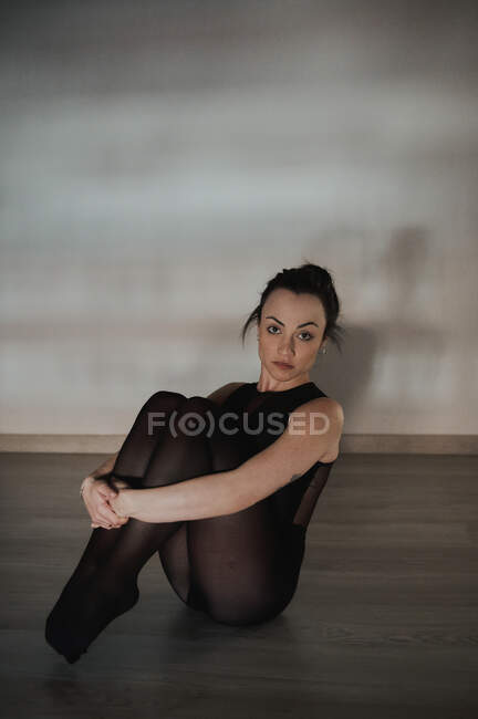 Jeune femme tendre en vêtements de sport assis sur le sol et regardant la caméra — Photo de stock