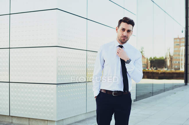 Hombre emprendedor en ropa formal con las manos en los bolsillos mirando a la cámara en la ciudad - foto de stock