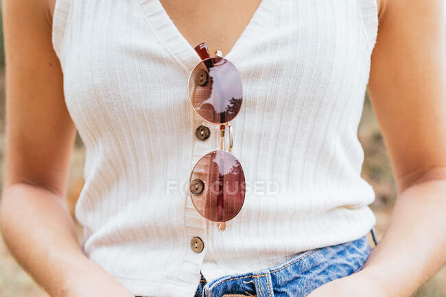 Вид на коріння анонімної жінки з сонцезахисними окулярами, що звисають з її сорочки — стокове фото
