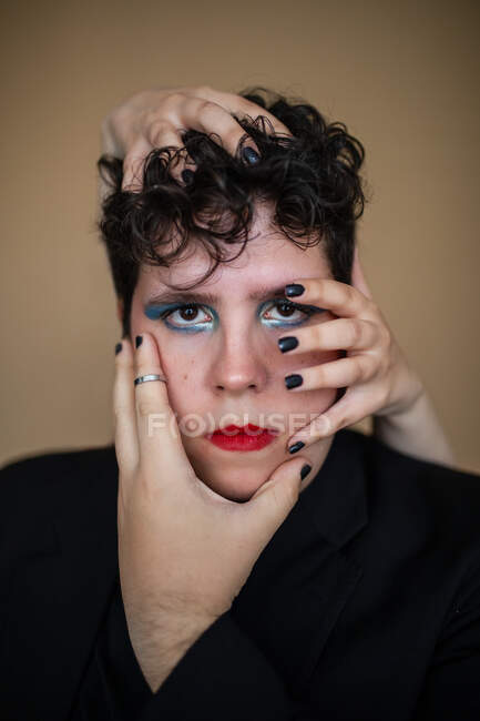 Homem sem emoção com maquiagem brilhante e lábios vermelhos tocados pela fêmea de colheita olhando para a câmera — Fotografia de Stock