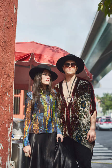Dal basso coppia elegante in abiti hipster tenendosi per mano mentre in piedi lungo la strada in estate — Foto stock