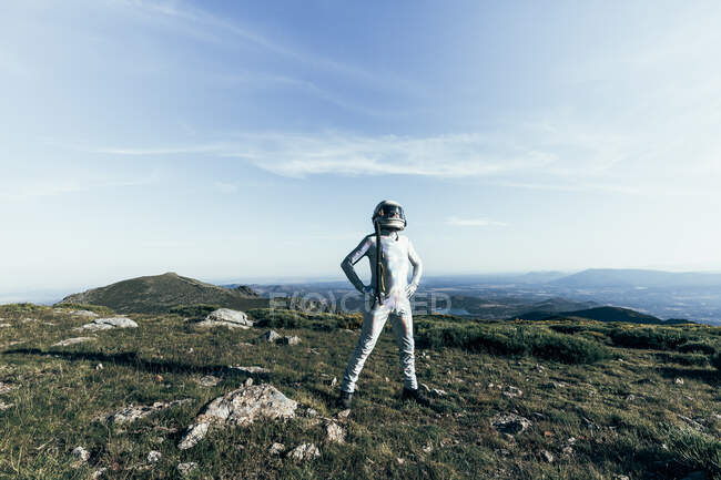 Astronaute masculin en combinaison spatiale et casque se tenant la main à la taille tout en se tenant debout sur l'herbe et les pierres dans les hautes terres — Photo de stock