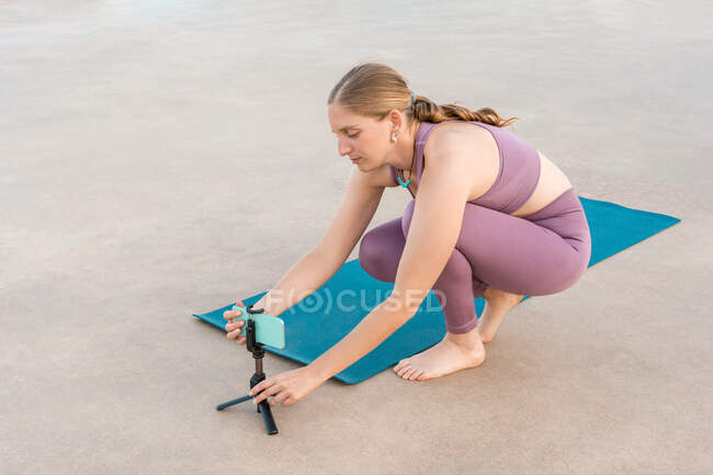 Ângulo alto de fêmea preparando telefone celular no tripé para fazer ioga durante a aula on-line — Fotografia de Stock
