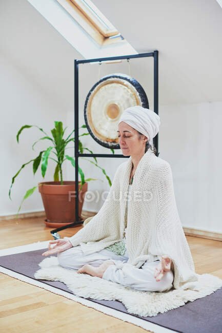 Mature female with closed eyes sitting with crossed legs on fluffy rug while practicing yoga at home — Stock Photo