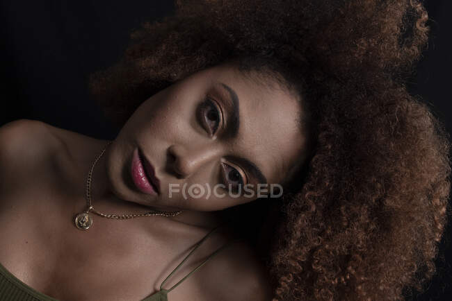 Charmantes afroamerikanisches Model mit lockigem Haar blickt im dunklen Studio in die Kamera — Stockfoto
