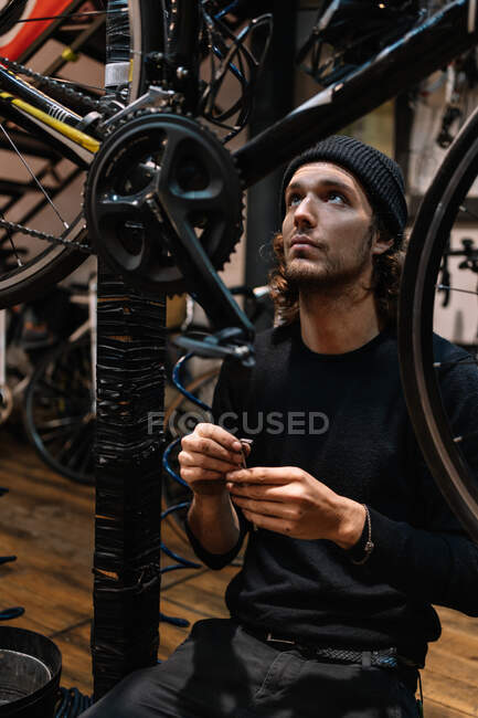 Occupé mâle maître fixation vélo moderne tout en travaillant dans l'atelier minable et la recherche vers le haut — Photo de stock