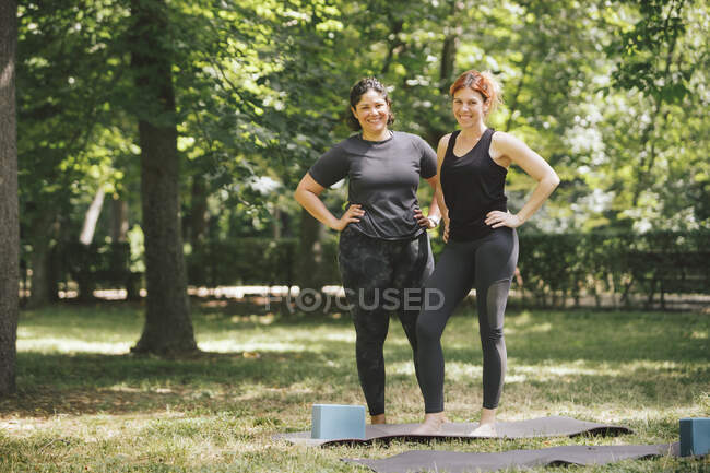 Conteúdo adulto melhores amigas do sexo feminino com as mãos na cintura olhando para a câmera depois de praticar ioga na luz solar — Fotografia de Stock