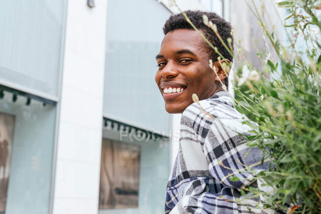 Side view of cheerful African American stylish male standing in city and looking at camera — Stock Photo