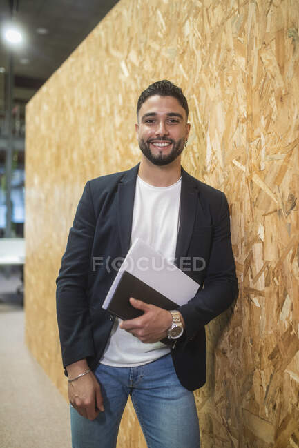 Задоволений чоловік-підприємець з документами, що стоять біля стіни в сучасному коворкінгу і дивляться на камеру — стокове фото