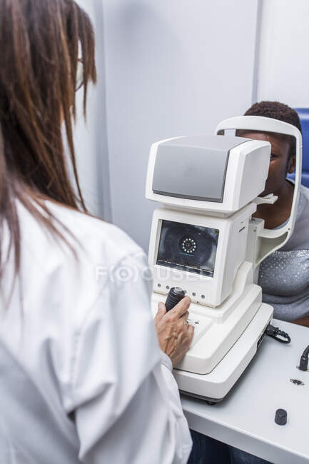 Оптометрист, що коригує ретинограф під час вивчення зору чорної жінки — стокове фото