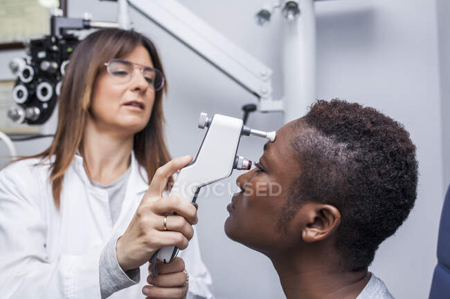 Optometrista usando um oftalmoscópio durante o estudo da visão de uma mulher negra — Fotografia de Stock
