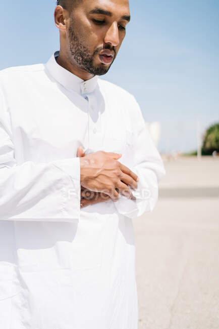 Garçon complet mâle islamique en vêtements blancs traditionnels debout sur le tapis et priant contre le ciel bleu sur la plage — Photo de stock
