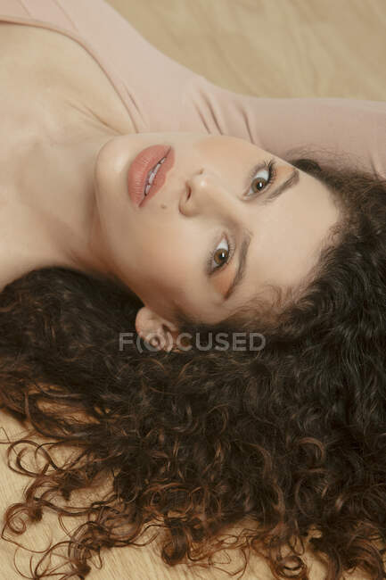 From above of tender female in beige bodysuit lying on wooden floor and looking at camera — Stock Photo
