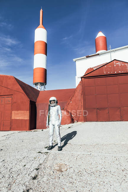 Homme en combinaison spatiale debout près du mur rouge de l'installation industrielle par une journée ensoleillée — Photo de stock