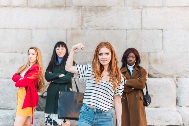 Selbstbewusste Frau zeigt Bizeps, während sie sich gegen eine Gruppe von multirassischen Frauen stellt, die ein Konzept von Girl Power zeigen — Stockfoto