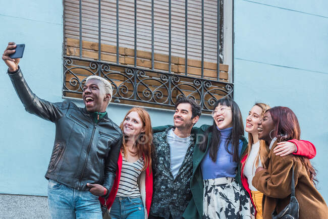 African American male taking selfie with smartphone with company of multiracial friends standing on street together — Stock Photo