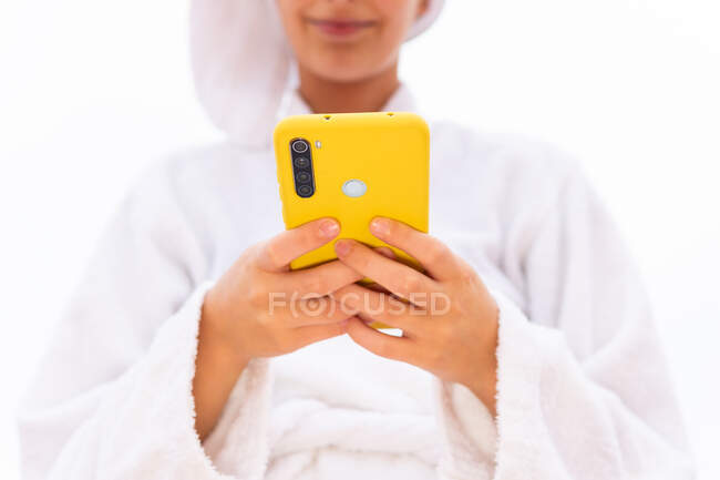 Crop Giovane femmina in accappatoio e asciugamano sorridente e la navigazione cellulare mentre riposano sul balcone dopo la doccia — Foto stock