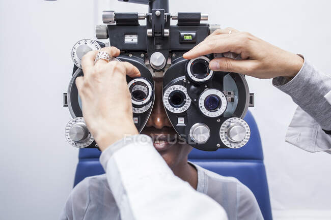 Оптометрист настраивает оптическое оборудование во время исследования зрения чернокожей женщины — стоковое фото