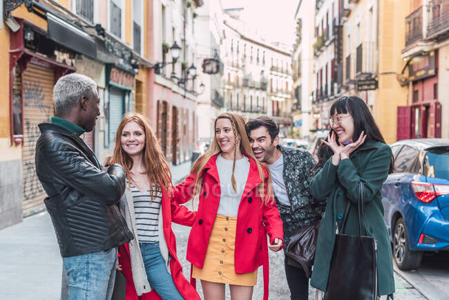 Compañía de amigos multirraciales felices en ropa elegante caminando juntos en la calle de la ciudad durante el fin de semana - foto de stock