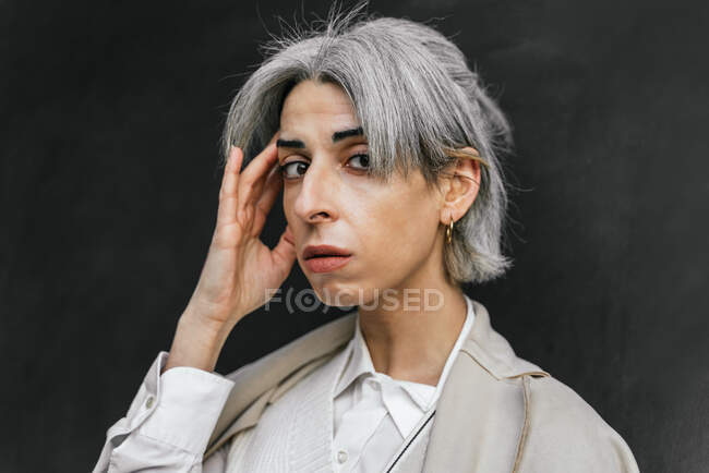 Впевнена стильна транссексуальна жінка з сірим волоссям торкається голови в місті вдень — стокове фото