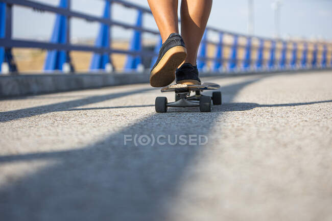 Women feet skating long board by an empty bridge at sunset, back view — Stock Photo