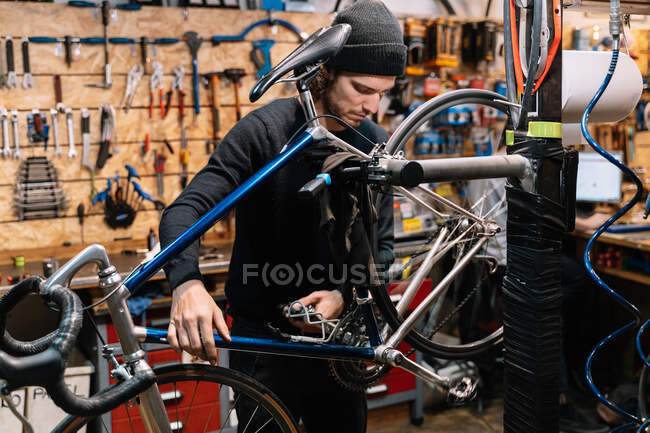 Vue latérale de la roue de réparation masculine grave du vélo tout en travaillant en atelier — Photo de stock