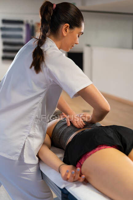 Вид сбоку на дружелюбную массажистку, улыбающуюся и массирующую плечи женщины во время работы в клинике физиотерапии — стоковое фото
