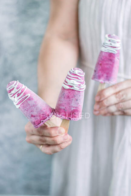 Faceless female in linen dress offering homemade blackberry yogurt popsicles with white topping — Stock Photo